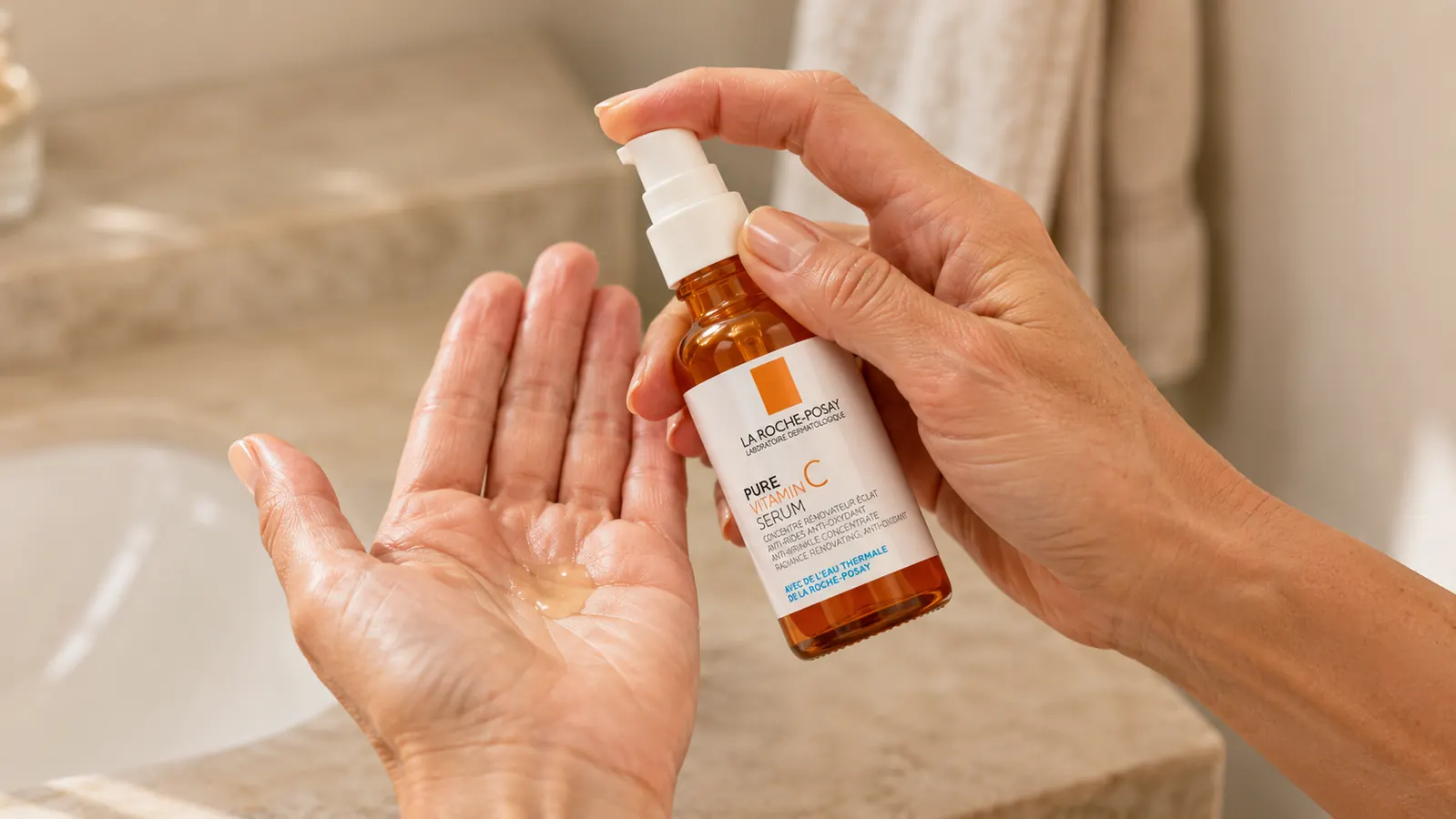 Woman's hand holding the La Roche-Posay vitamin C serum bottle, pressing the pump over an open palm